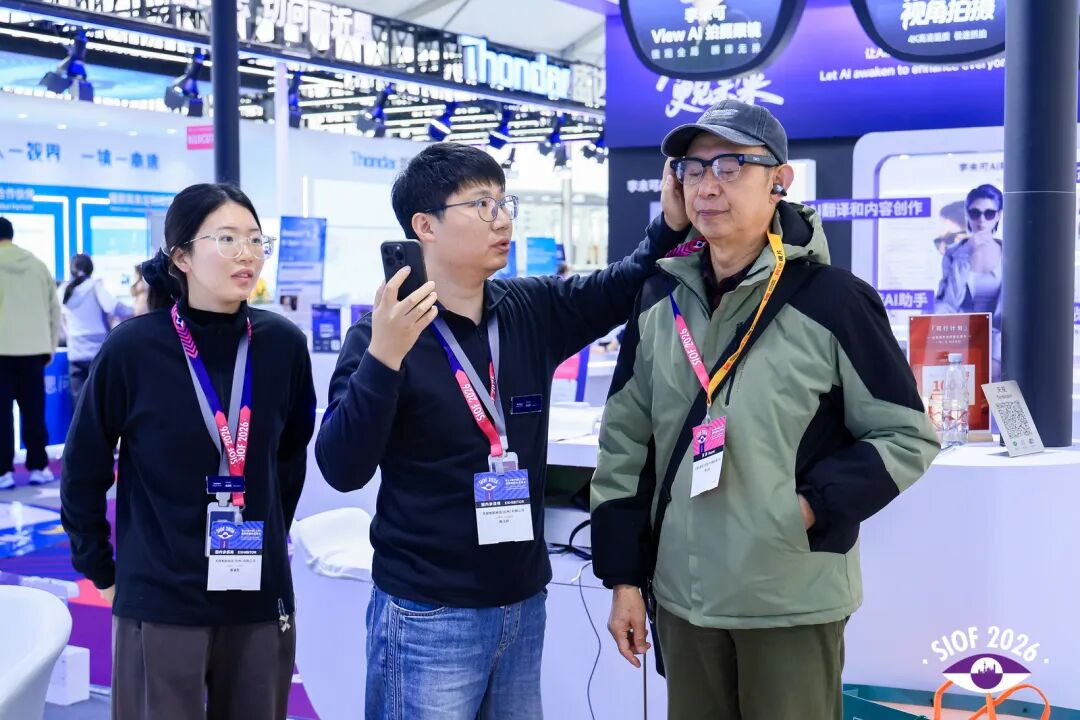 A booth featuring visual assistance technology is presented by three people, with a cell phone prominently displayed in front.